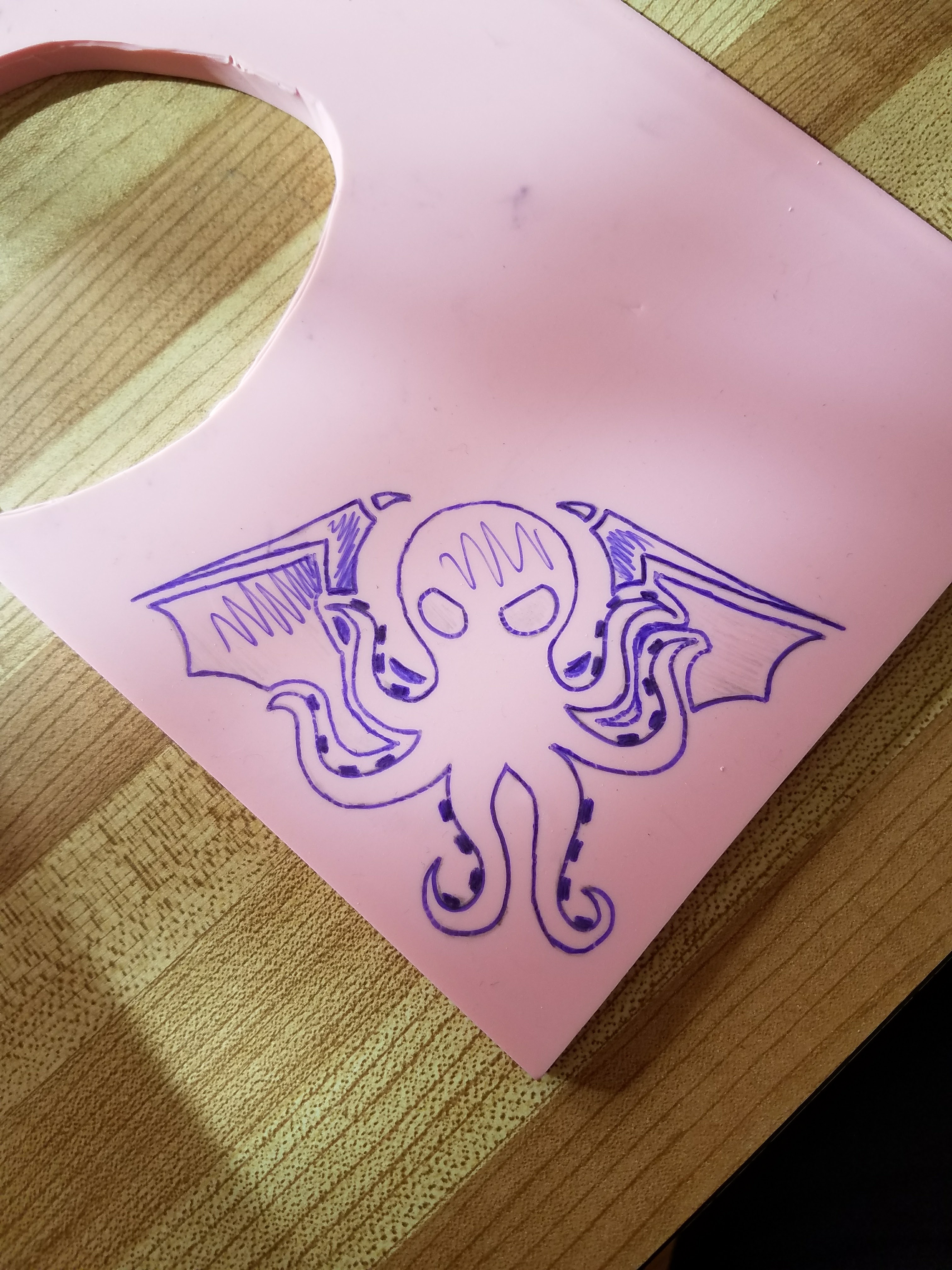 A block of pink rubber with a picture of Cthulhu's head and wings drawn on it in blue pen.